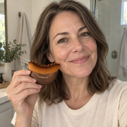 Dewmere palm-sized facial brush shown beside a woman's face — AI lifestyle illustration